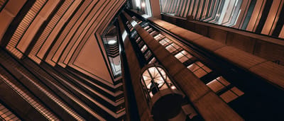 A glowing glass elevator ascends through the center of a towering, geometric modern atrium.