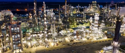 A dramatic aerial view of an illuminated oil refinery operating at night.