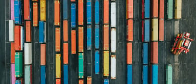 An aerial top-down view of brightly colored shipping containers arranged in straight, chart-like rows at a logistics hub.