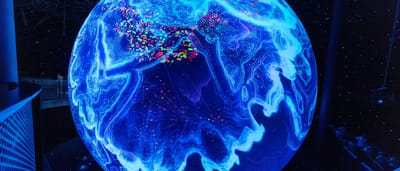 A glowing blue digital projection of the Earth covered in data points in a dark room.