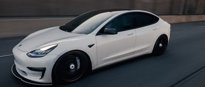 A white Tesla Model 3 driving smoothly along a highway at dusk.