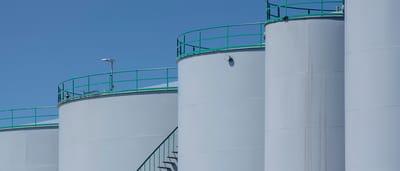 Large industrial white storage tanks stand against a clear blue sky.