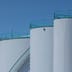 Large industrial white storage tanks stand against a clear blue sky.