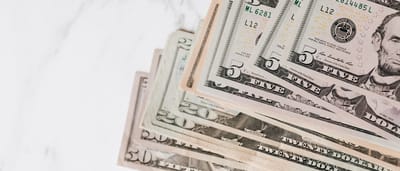 A close-up view of a stack of United States dollar banknotes in various denominations resting on a marble surface.