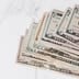A close-up view of a stack of United States dollar banknotes in various denominations resting on a marble surface.