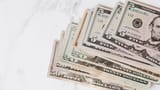 A close-up view of a stack of United States dollar banknotes in various denominations resting on a marble surface.