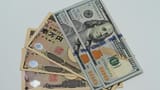 A close-up view of United States one hundred dollar bills resting on top of Japanese ten thousand yen notes.