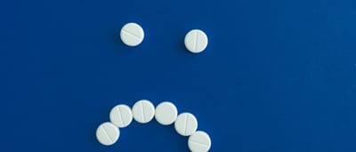 White round pills arranged in the shape of a frowning sad face on a solid blue background.