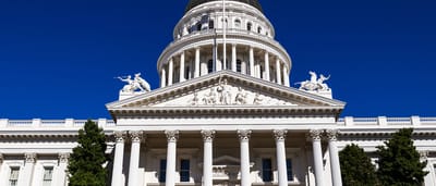The pristine white facade and dome of the California State Capitol building under a clear blue sky.