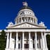 The pristine white facade and dome of the California State Capitol building under a clear blue sky.