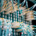 Close-up of bright teal fiber optic cables plugged into a high-density data center network switch.
