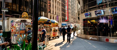 Pedestrians and street vendors walk past the exterior of the Nasdaq MarketSite building in a sunny Times Square.