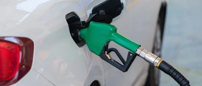 A green fuel pump nozzle inserted into the gas tank of a white car at a service station.