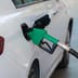 A green fuel pump nozzle inserted into the gas tank of a white car at a service station.