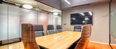 An empty wooden boardroom table surrounded by sleek executive chairs inside a modern corporate office.