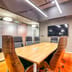 An empty wooden boardroom table surrounded by sleek executive chairs inside a modern corporate office.