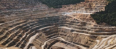 An expansive aerial view of a massive, terraced open-pit mine under a bright sky.
