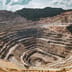 An expansive aerial view of a massive, terraced open-pit mine under a bright sky.