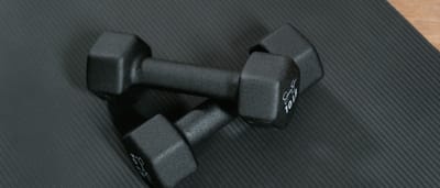 A pair of identical black dumbbells resting on a textured black gym mat.