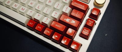 A close-up of a custom mechanical keyboard featuring prominent red Backspace and Delete keys.